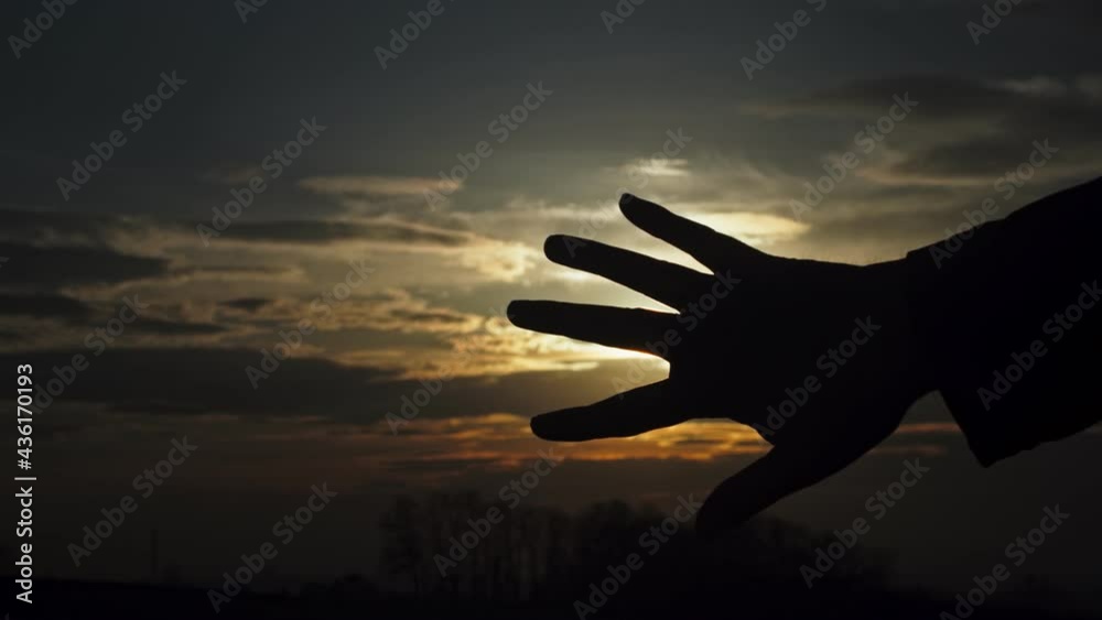 Silhouette of hand in front of sunset, playing with the light between fingers, right side