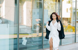 Stylish lady in black-white colors outdoor. Fashionable female manager leaves her modern office. Street fashion.