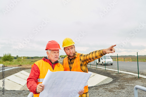 Architekt und Vorarbeiter mit Bauzeichnung auf Baustelle