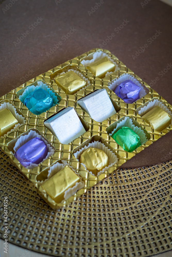 wrapped luxury chocolates in various colours for different flavours in a golden container on a brown background. wrapped luxury chocolates in various colours for different flavours in a golden container on a brown background.