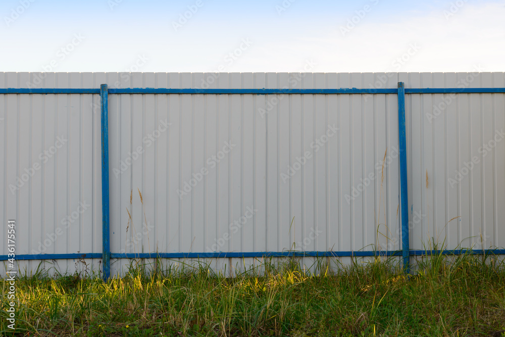 Obraz premium Grey metal perforated fence with blue posts in a green clearing