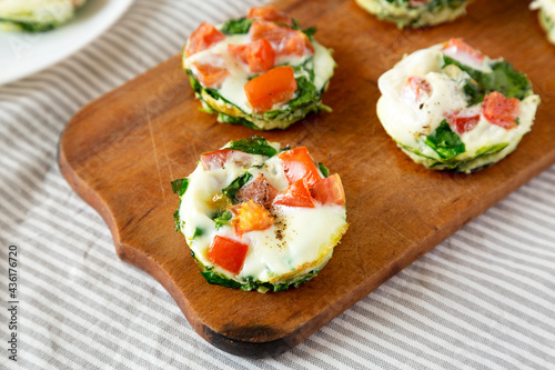 Homemade Egg White Breakfast Cups with Spinach and Tomato on a rustic wooden board, low angle view.