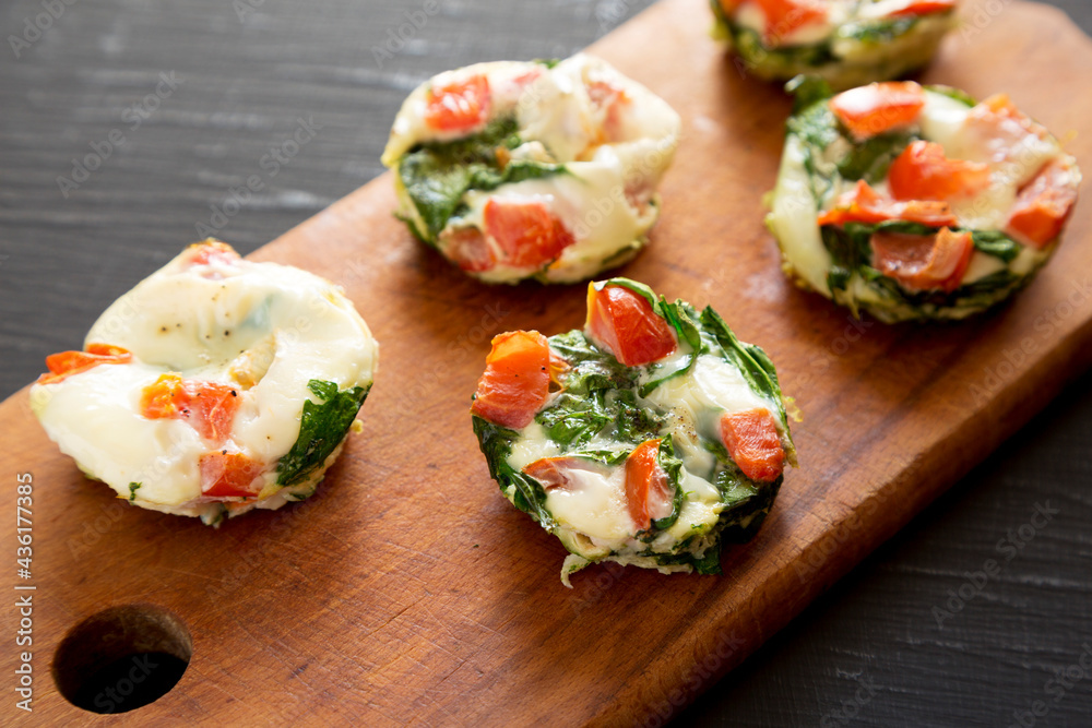 Homemade Egg White Breakfast Cups with Spinach and Tomato on a rustic wooden board on a black background, side view. Homemade Egg White Breakfast Cups with Spinach and Tomato on a rustic wooden board on a black background, side view.