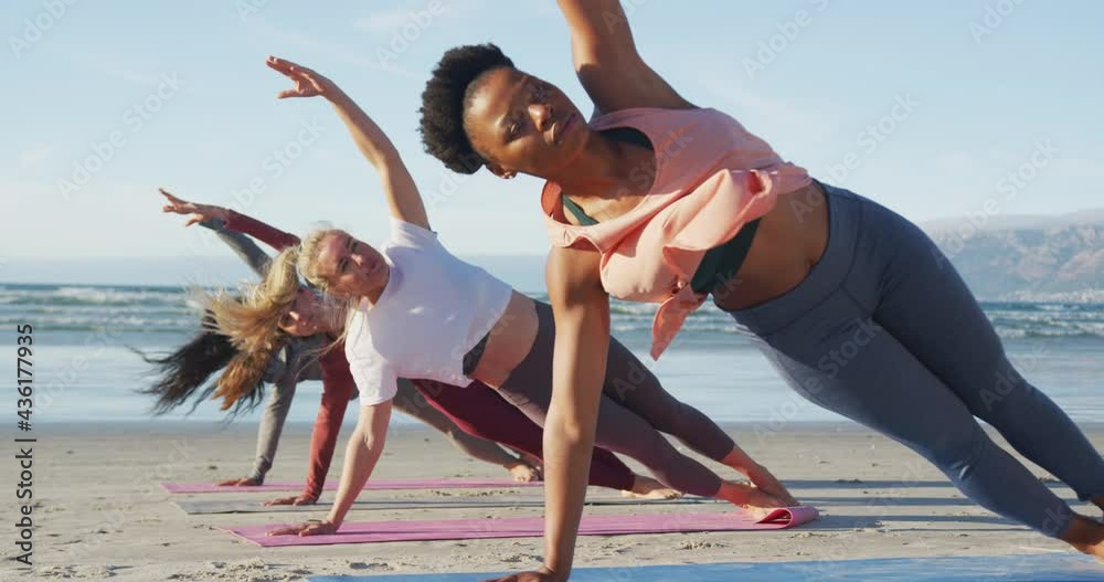 Group of diverse female friends practicing yoga at the beach