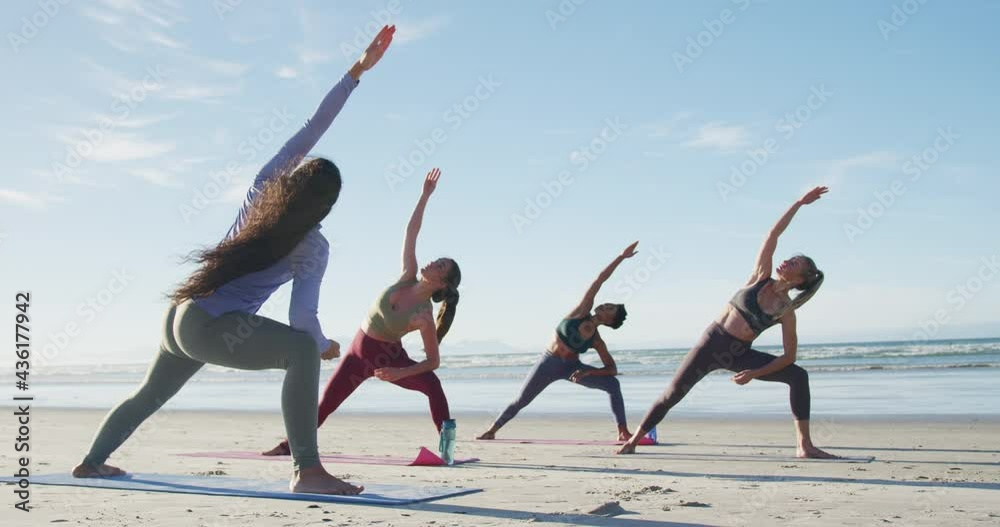 Group of diverse female friends practicing yoga at the beach