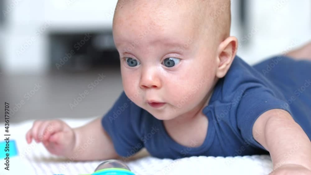 beautiful baby infant with blue eyes lying on the floor on the belly looking wondering at toys beautiful baby infant with blue eyes lying on the floor on the belly looking wondering at toys