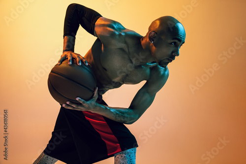 Fototapeta Naklejka Na Ścianę i Meble -  Close-up portrait of african-american male basketball player posing in neon light on orange background.