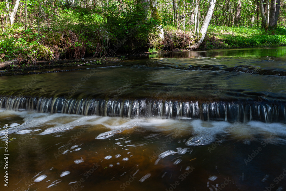 Cascading waterfall cascades in Estonia in green light at summertime