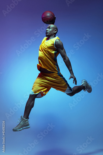 Handsome african-american male basketball player in action and motion in neon light on blue background. Concept of healthy lifestyle, professional sport. © master1305