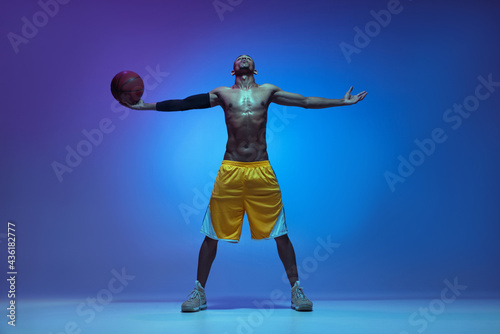 Sportive athletic african-american male basketball player posing in neon light on blue background. © master1305