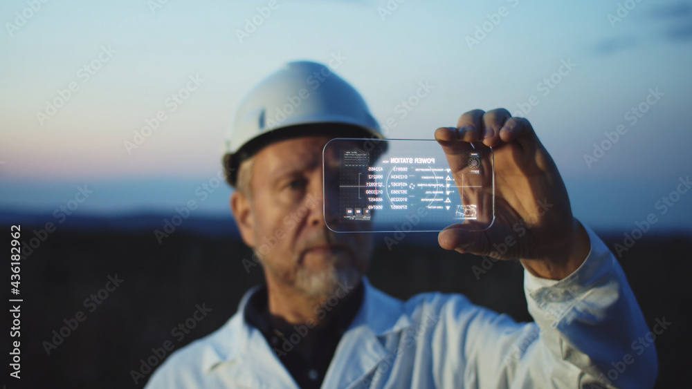 Adult bearded man scientist using high tech smartphone to diagnose online the workflow on modern windmill farm. Beautiful sunset sky on background. The newest technology trend of communication. - obrazy, fototapety, plakaty 