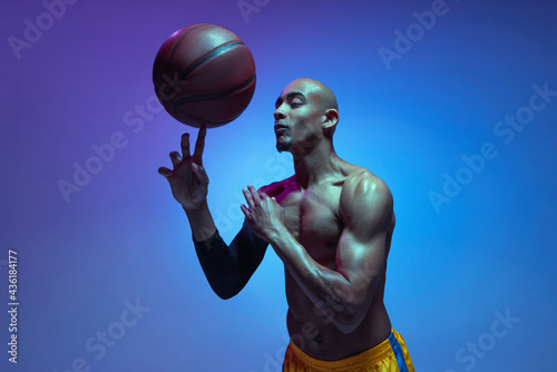 Strong muscular african-american male basketball player training in neon light on orange background. © master1305