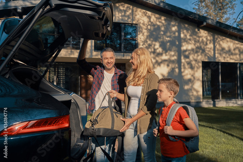 Happy young family packing stuff into the car and smiling while standing near house