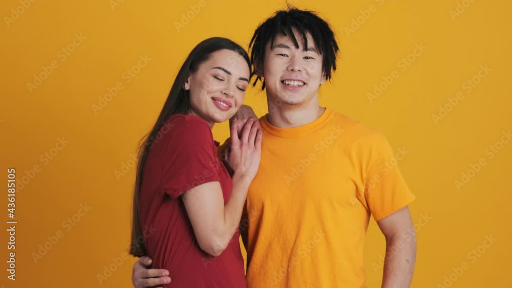 Happy multinational couple man and woman are posing to the camera standing isolated over yellow wall in the studio Happy multinational couple man and woman are posing to the camera standing isolated over yellow wall in the studio