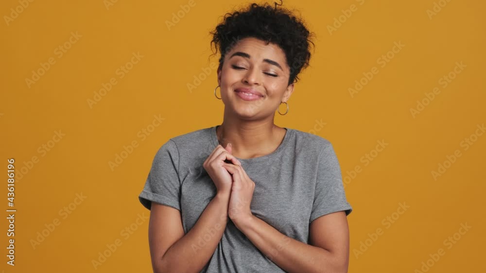 A smiling american woman wearing gray basic T-shirt is looking at something cute standing isolated over yellow wall in the studio A smiling american woman wearing gray basic T-shirt is looking at something cute standing isolated over yellow wall in the studio