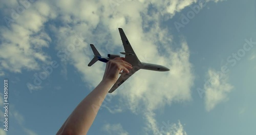The boy holds with his hand a miniature model of an airplane near the turbines and depicts flight. The toy flies in a picturesque sky with white feather clouds. The child imagines that he is a pilot