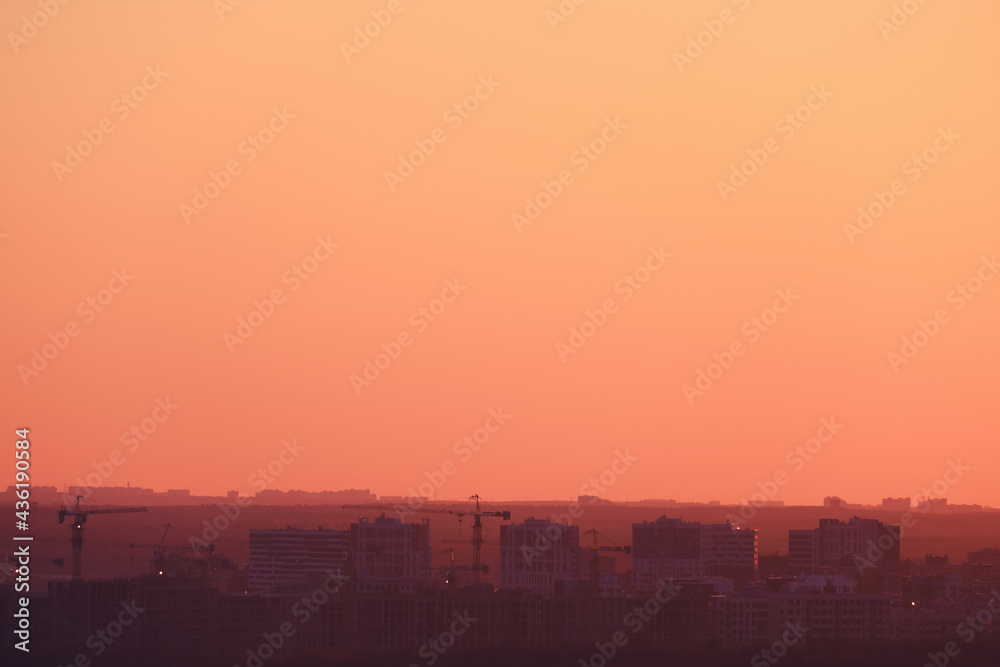 Buildings in a city under construction against the background of an orange sunset sky, copy space