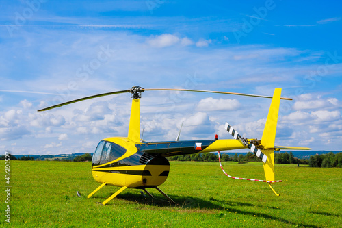 Modern small light helicopter on a grassy field against the blue sky.