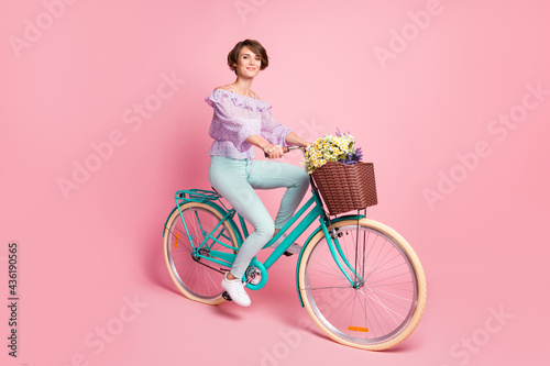 Photo of positive lady drive bike deliver flowers wear violet blouse pants shoes isolated pink color background © deagreez