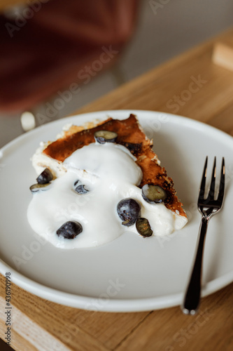 San Sebastian or basque cheesecake with blueberry and vanilla cream on a white plate with a dessert fork