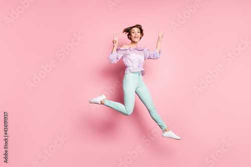 Full size photo of young happy charming excited positive girl jumping showing v-sign isolated on pink color background © deagreez