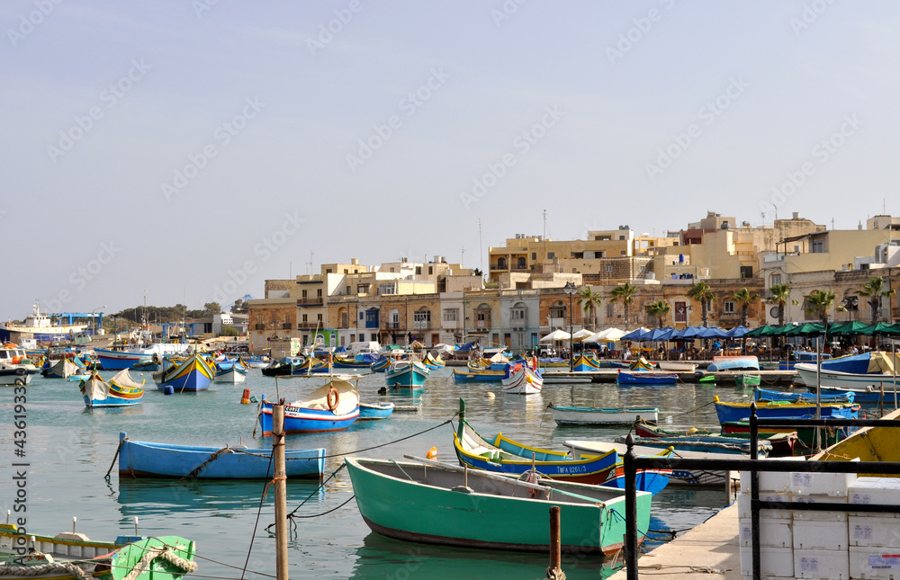 Overlooking the harbor with traditional blue fishing boats and the ancient buildings of Marsaxlokk. Marsaxlokk is a small, traditional fishing village in the South Eastern Region of Malta.