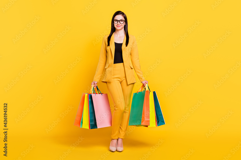 Full length photo of young attractive woman happy positive smile hold shopping bags sale isolated over yellow color background Full length photo of young attractive woman happy positive smile hold shopping bags sale isolated over yellow color background