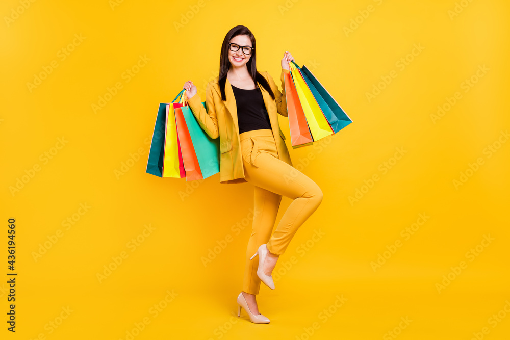 Photo of pretty adorable young lady dressed formal blazer glasses smiling holding colorful bags isolated yellow color background Photo of pretty adorable young lady dressed formal blazer glasses smiling holding colorful bags isolated yellow color background