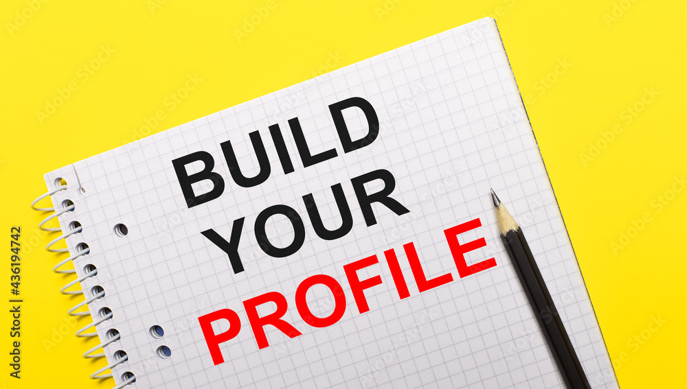 Obraz premium White notebook with inscription BUILD YOUR PROFILE written in black pencil on a bright yellow background.