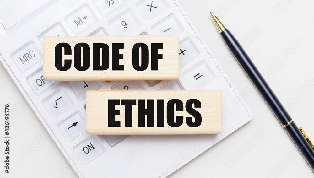 Wooden blocks with the text CODE OF ETHICS lie on a light background on a white calculator. Nearby is a black handle. Business concept Wooden blocks with the text CODE OF ETHICS lie on a light background on a white calculator. Nearby is a black handle. Business concept