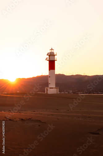 Sunset picture captured in "Fangar" Beach with a beautiful lighthouse and the sun hiding it behind the mountains. Ebro Delta, Tarragona, Spain.