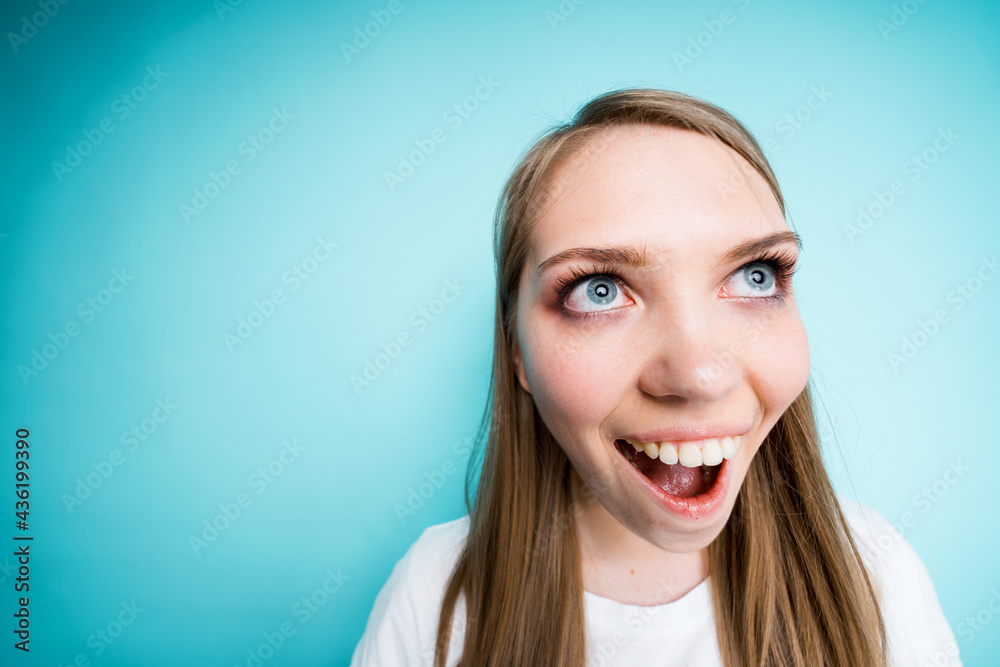 Close-up photo. Happy beautiful girl smiles broadly while standing on a blue background. Fish eye shot Close-up photo. Happy beautiful girl smiles broadly while standing on a blue background. Fish eye shot