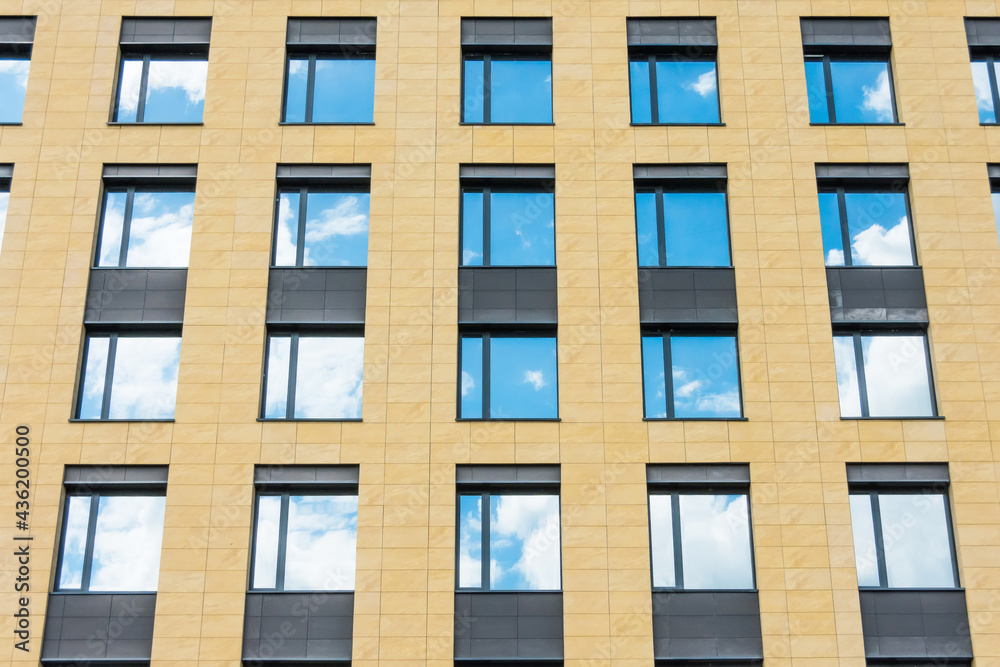 Separate windows office building yellow wall with clouds sky mirror.