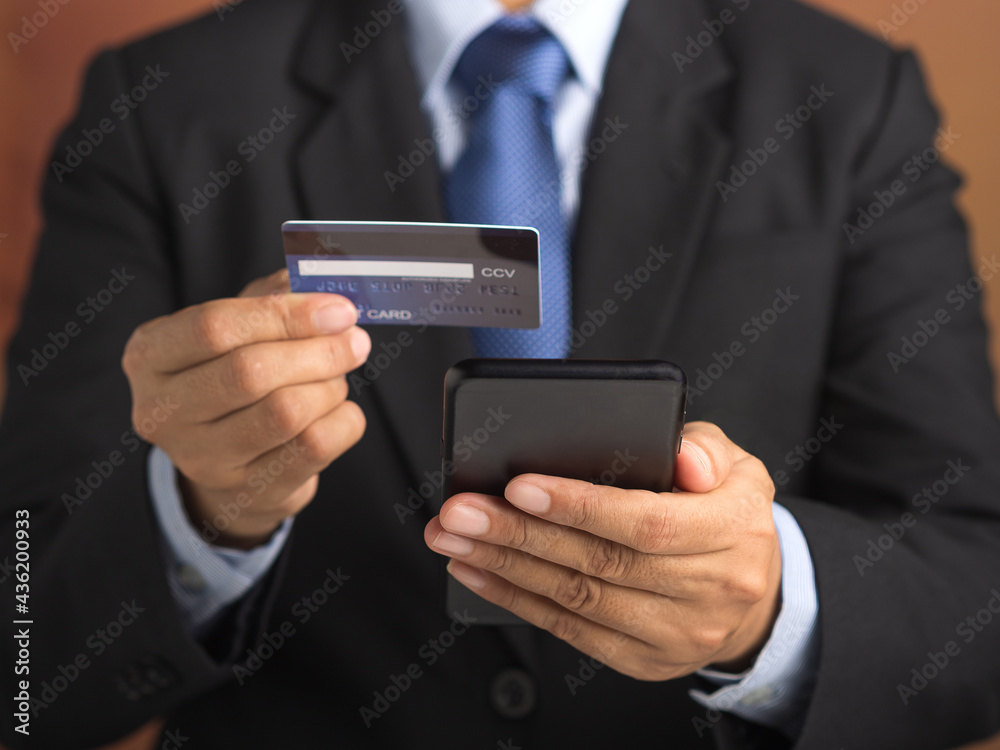 Businessman using a smartphone with a credit card while standing in the studio with a vintage background. Close-up photo. Space for text. Communication, technology, e-commerce, and business concept Businessman using a smartphone with a credit card while standing in the studio with a vintage background. Close-up photo. Space for text. Communication, technology, e-commerce, and business concept