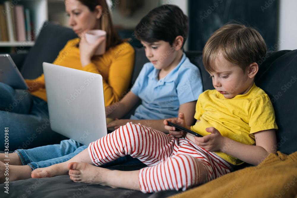 mother with her kids using laptop computer, while sitting on a sofa at home mother with her kids using laptop computer, while sitting on a sofa at home