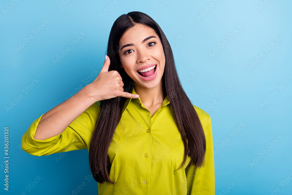 Photo of young girl happy positive smile show finger call phone sign talk speak isolated over blue color background Photo of young girl happy positive smile show finger call phone sign talk speak isolated over blue color background