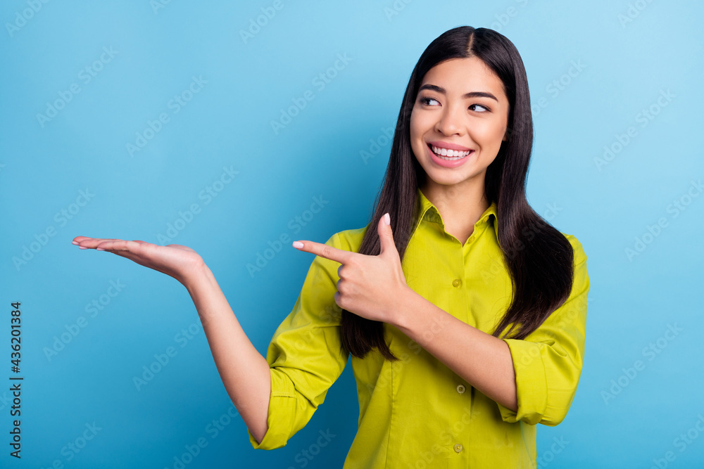 Photo of young girl happy positive smile look indicate finger product promotion select suggest isolated over blue color background Photo of young girl happy positive smile look indicate finger product promotion select suggest isolated over blue color background