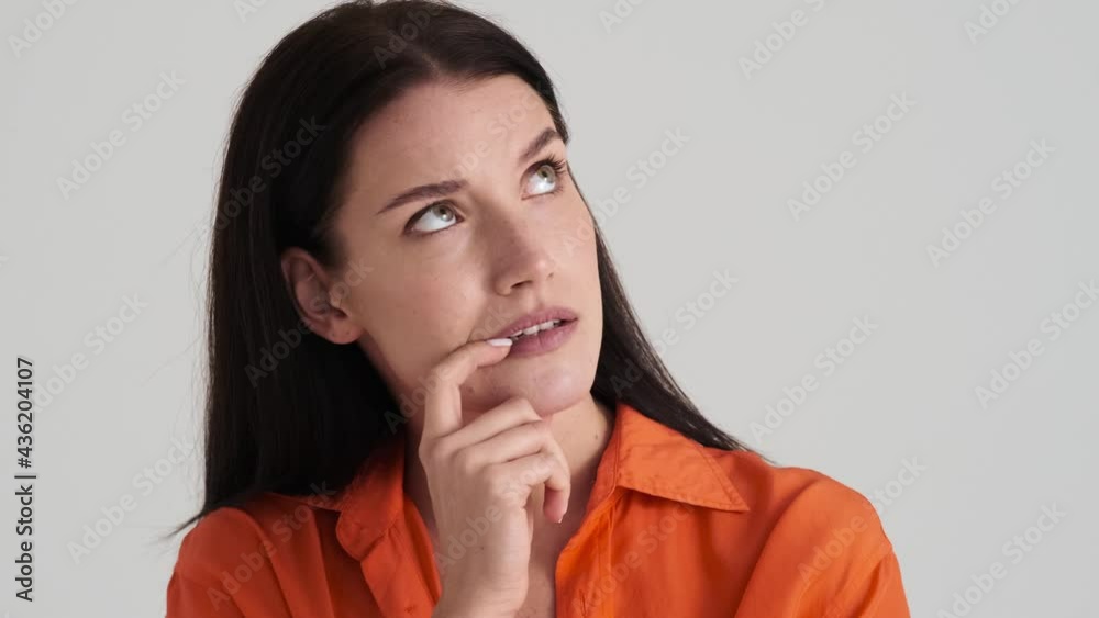 A serious woman is thinking about something standing isolated over grey wall in the studio A serious woman is thinking about something standing isolated over grey wall in the studio