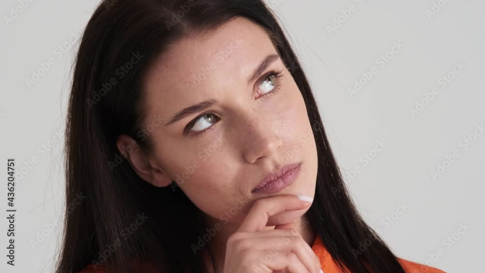 A close-up view of a serious woman is thinking about something standing isolated over grey wall in the studio A close-up view of a serious woman is thinking about something standing isolated over grey wall in the studio