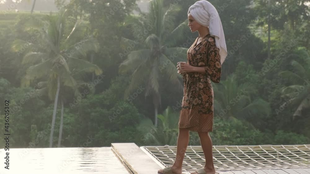girl in a light robe with a cup of coffee in the morning in the jungle enjoying the sunrise,women in robe to walk to the swimming pool on tropical pool.relaxing and recreation at summer time.honeymoon