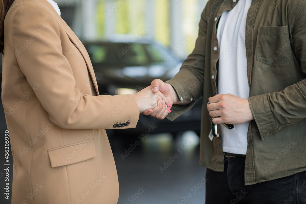 Salesperson selling cars at car dealership. Close up of dealer giving key to new owner.