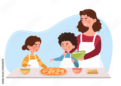Young mother is helping little son and daughter to cook pizza in the kitchen