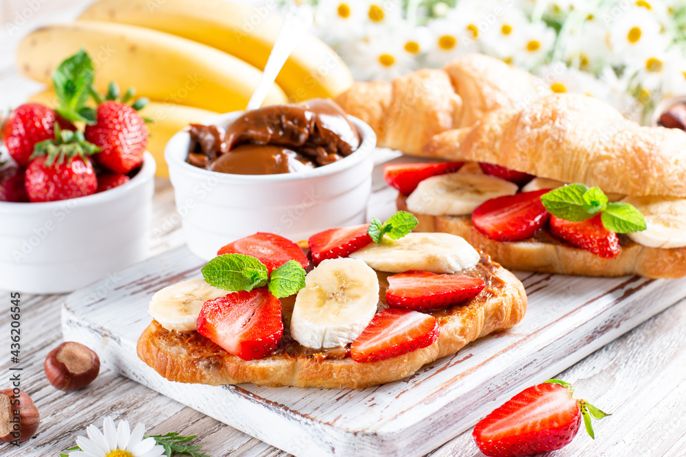 Delicious breakfast with fresh croissants, chocolate, banana and strawberry on table. French pastry