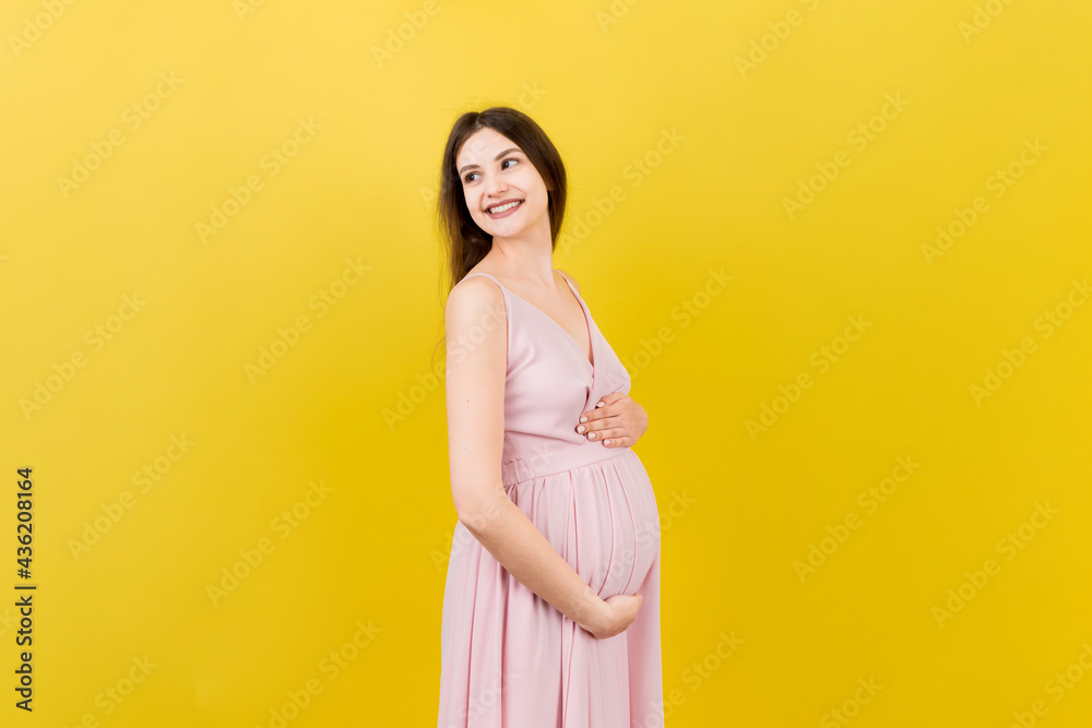 Happy pregnant woman touching her abdomen at Colored background. Future mother. Expecting of a baby. Copy space Happy pregnant woman touching her abdomen at Colored background. Future mother. Expecting of a baby. Copy space