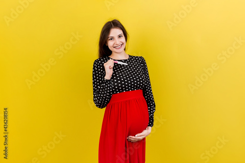 positive pregnancy test with two stripes against happy pregnant woman abdomen at Colored background. Future mother in gray dress. Pregnancy surprise. Copy space © sosiukin