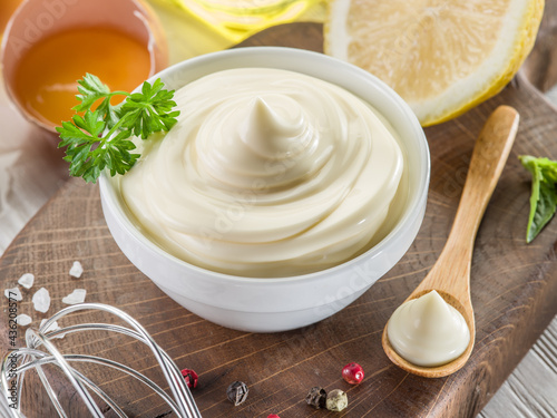 Bowl with mayonnaise sauce in the centre and mayonnaise ingredients around it on wooden table. Close-up. photo
