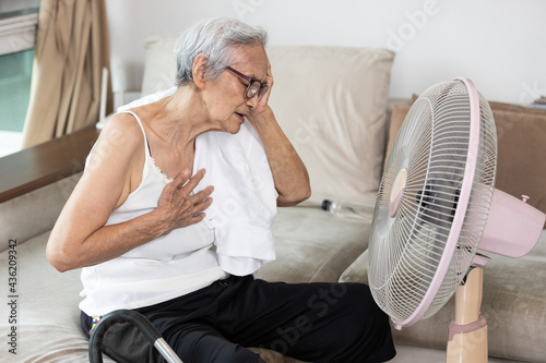 Overheated asian old people having a headache,chest tightness,heartbeat fast from high temperature,hot summer weather,elderly grandmother with symptom of heat stroke,Tired senior woman sitting at home