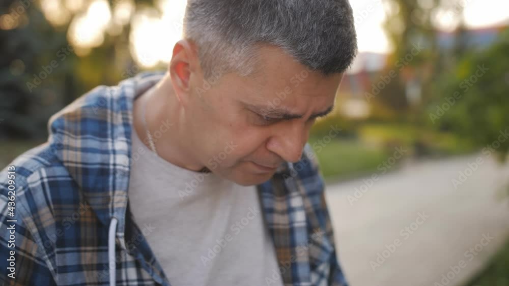 Close-up of a middle-aged man working on a laptop in a park area. Close-up of a middle-aged man working on a laptop in a park area.