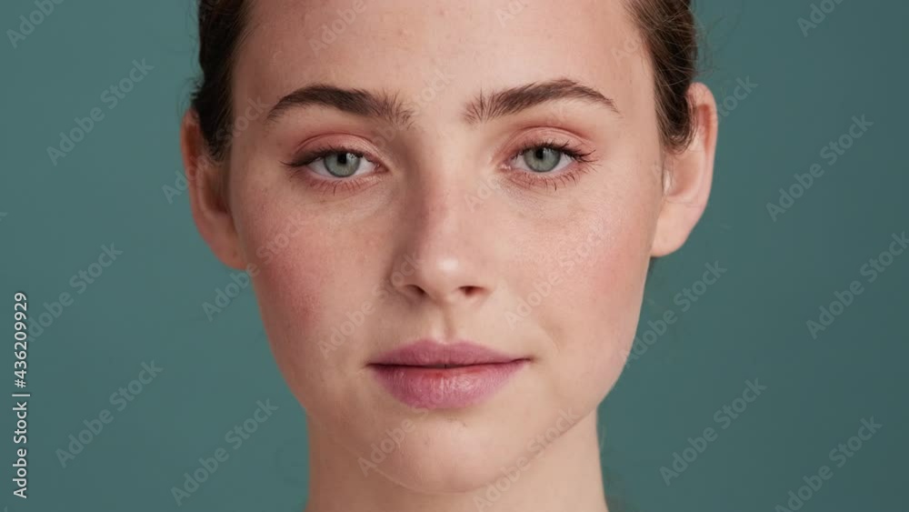 A close-up view of a pleased woman is looking to the camera standing isolated over grey wall in the studio