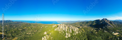 View from above, stunning aerial view of a valley surrounded by some granite mountains, green vegetation and the mediterranean sea in the distance. San Pantaleo, Sardinia, Italy. © Travel Wild